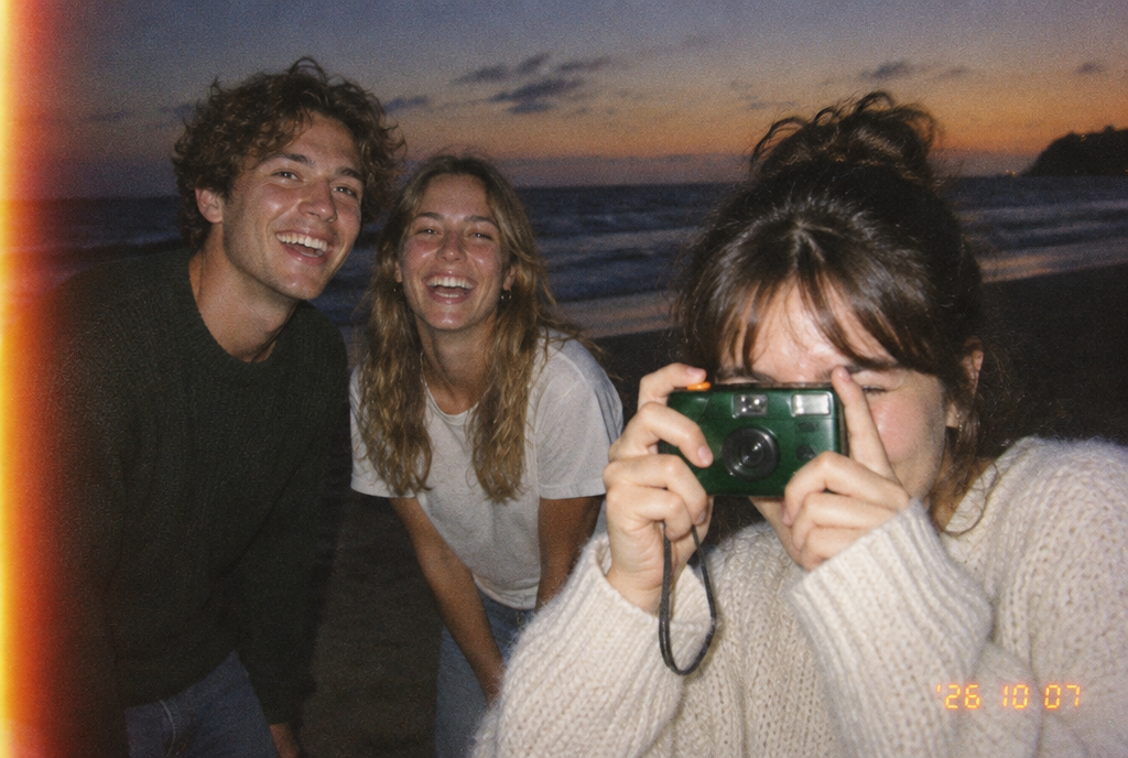 Friends on a beach at dusk, shooting with a kept. camera